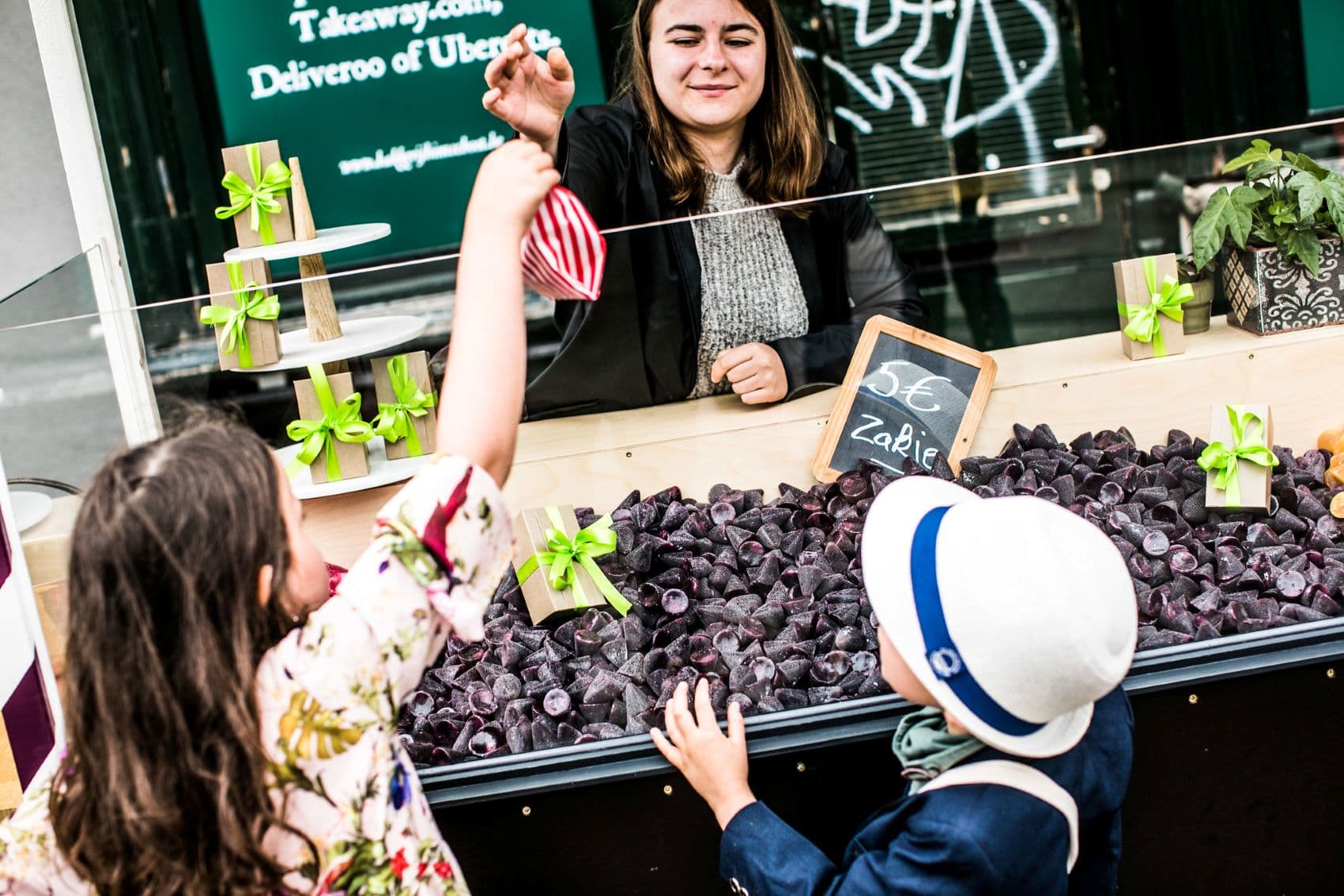 Verkäuferin in Gent reicht 2 Kindern eine Tüte Cuberdons über die Theke