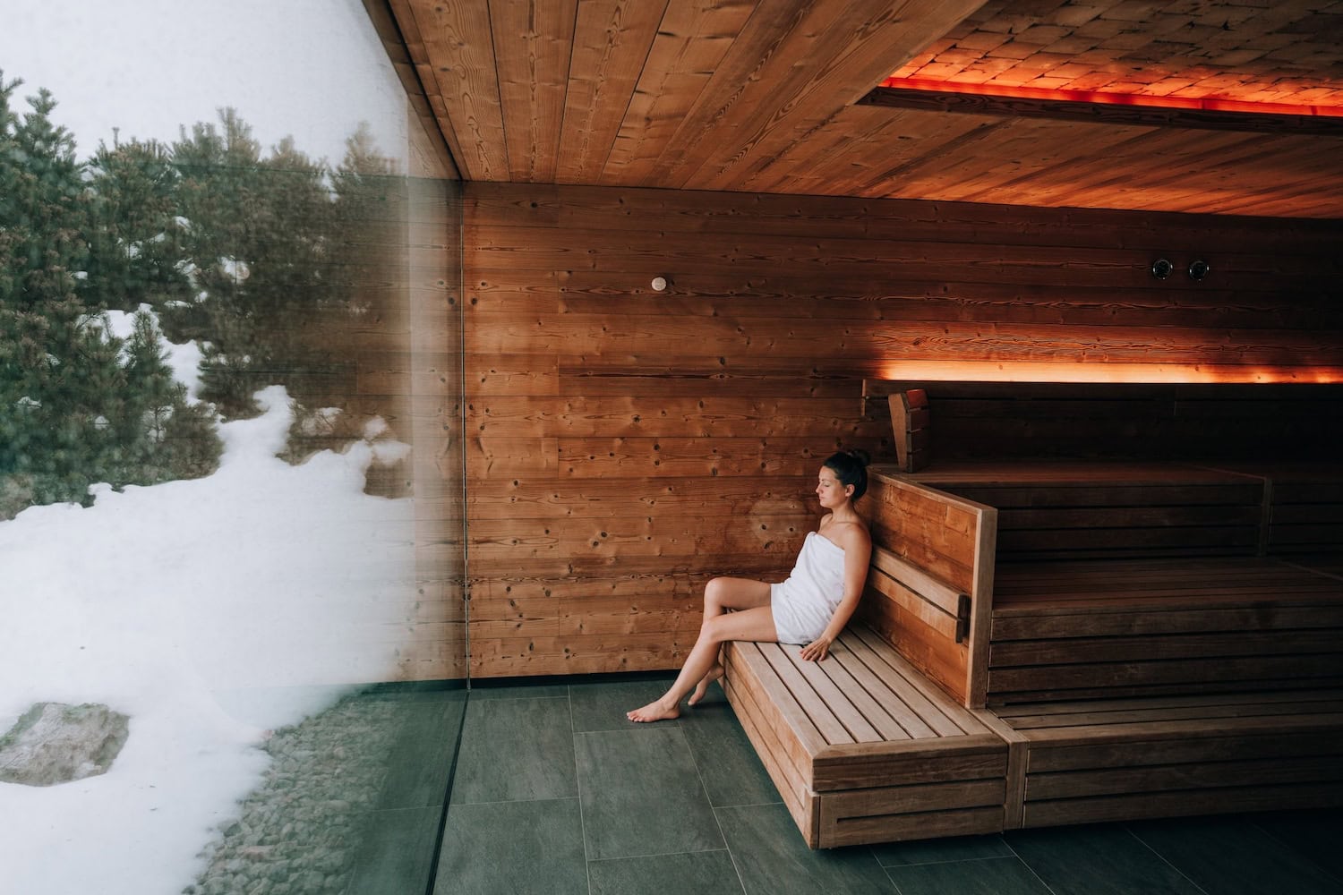 Frau sitzt in der Sauna mit Schnee vor der Fensterscheibe