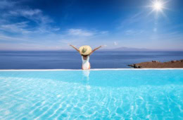 Eine Frau sitzt am Rand eines Pools und blick aufs Meer. Laut einer Umfrage gönnen sich immer mehr Leute im Urlaub Luxus!