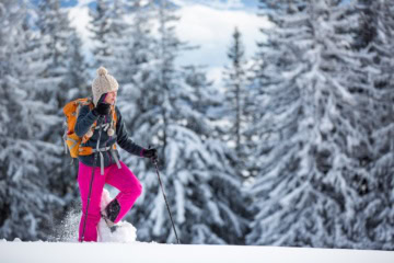 Frau mit Rucksack und Schneeschuhen vor schneebedecktem Wald