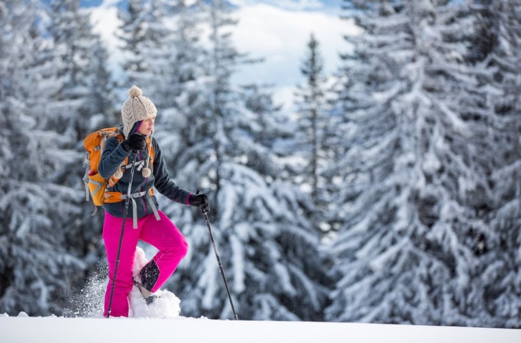 Frau mit Rucksack und Schneeschuhen vor schneebedecktem Wald