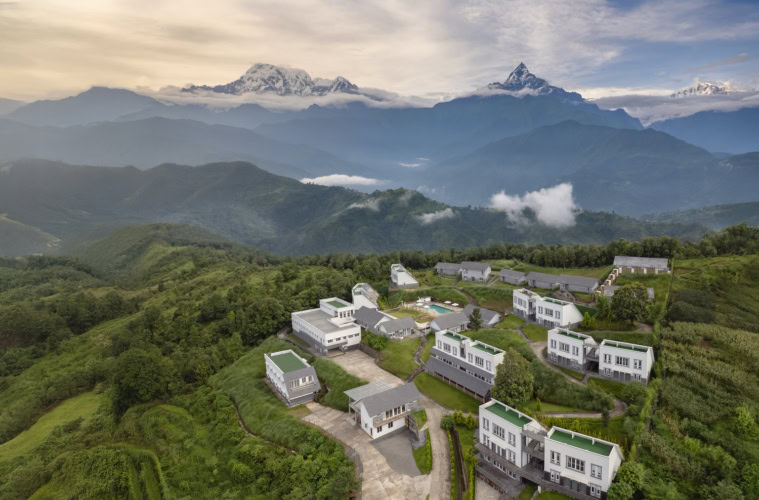 Himalayan Hideaway Resort Pokhara - Luftaufnahme, verschiedene Gebäude und Villen inmitten der Berglandschaft des Himalaya, viel Grün drum herum und in der Ferne das Annapurna Massiv.