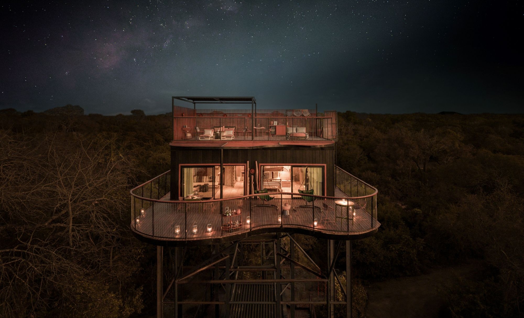Horizon Terrace Suite im Anantara Tented Camp Kafue River in Sambia bei Nacht, mit erhöhtem Schlafplatz unter dem Sternenhimmel und beleuchteter Terrasse.
