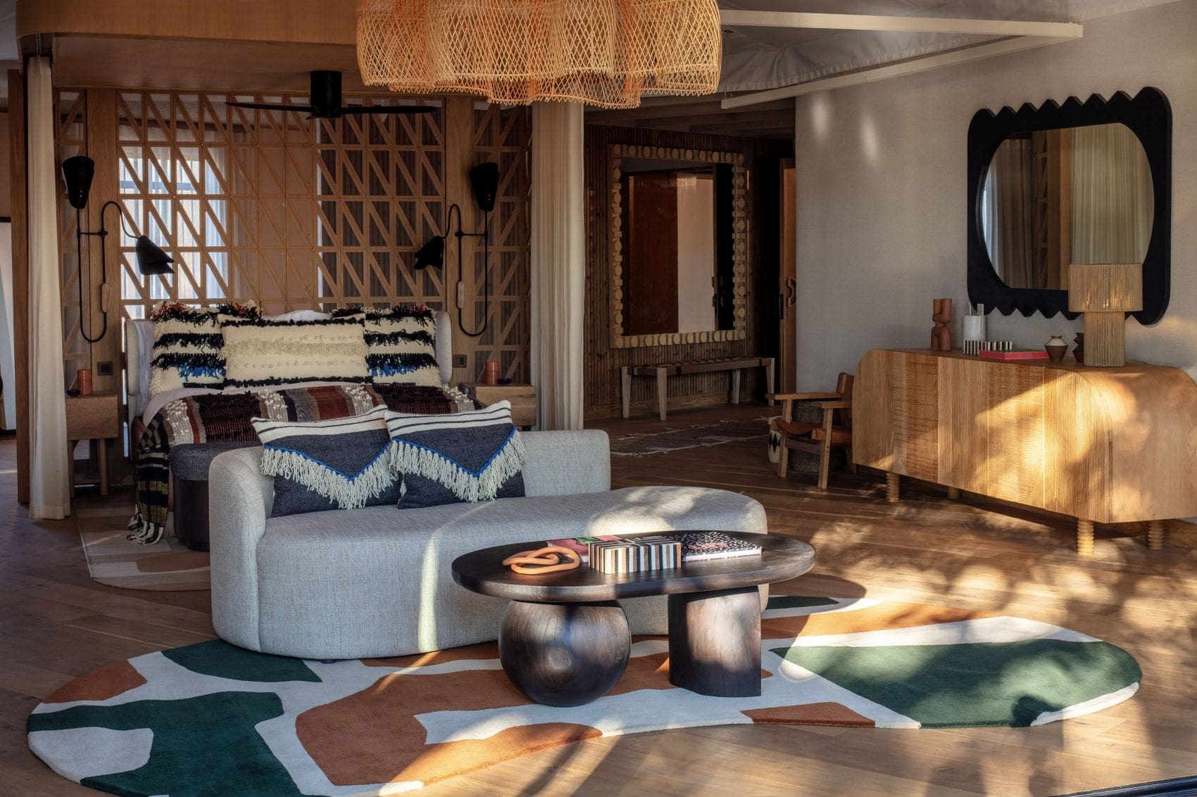 Schlaf- und Wohnbereich im Anantara Tented Camp Kafue River in Sambia mit Holzgitterwand, gemusterten Textilien, geschwungener Sitzbank und großer Flechtleuchte.