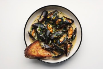 Miesmuscheln mit Cider, Schalotten und Lauch auf einem Teller.