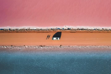 Luftaufnahme einer Straße, darauf ein Auto und zwei Personen. Nördlich der Straße ist ein rosa See, südlich ein blauer See