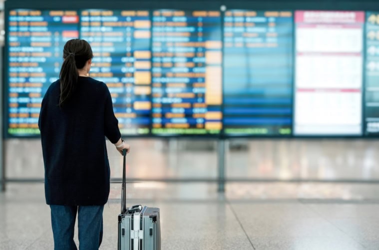 Frau mit Koffer am Flughafen vor der Abflugsanzeige