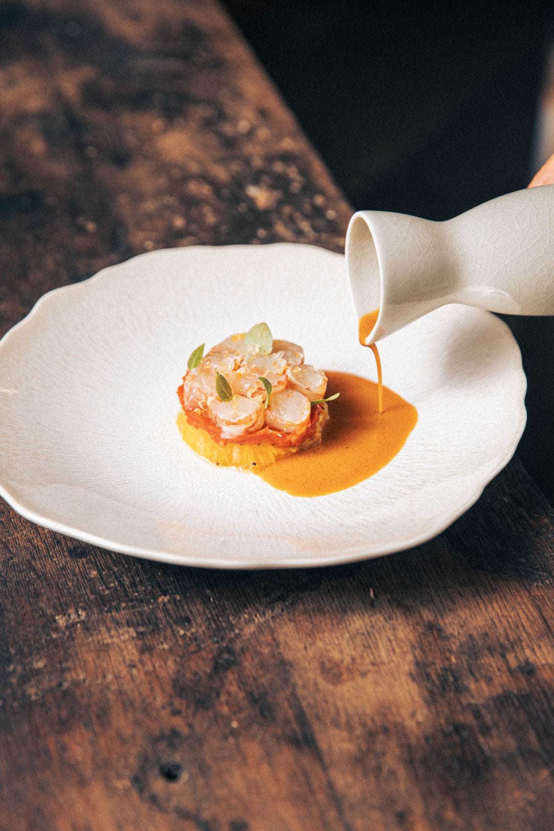 Meeresfrüchte, veredelt mit frischen Kräutern, während eine cremige, orangefarbene Sauce darüber gegossen wird