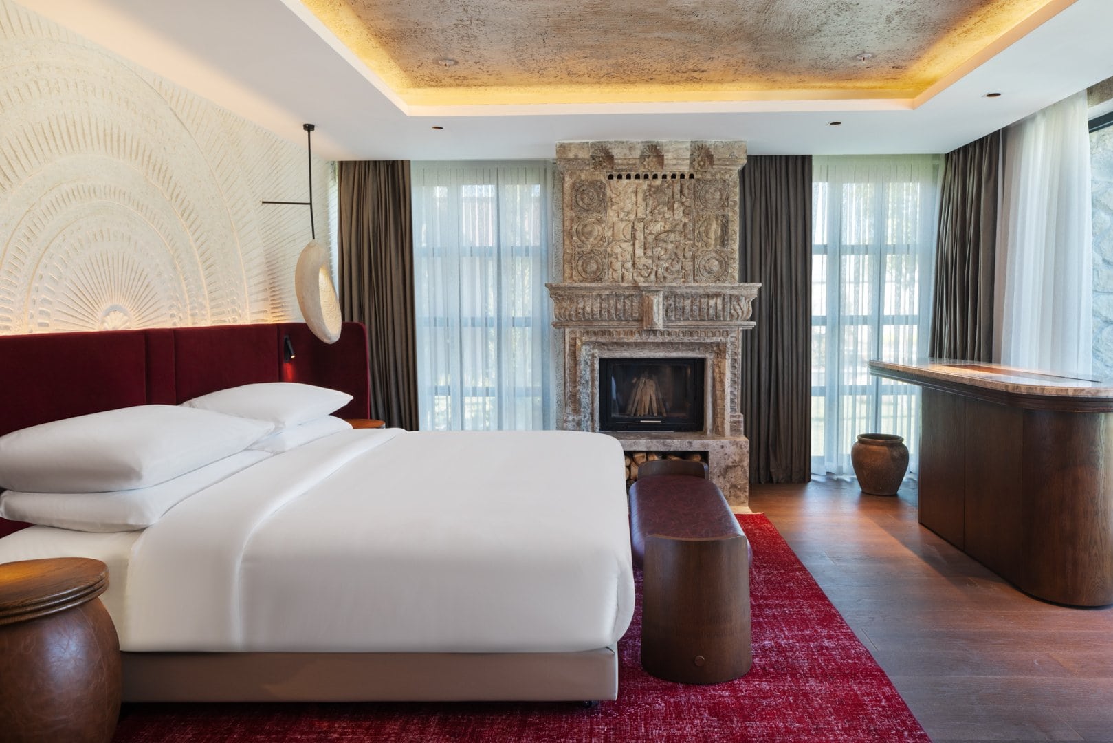Hotelzimmer im Fortuna of Cappadocia mit Doppelbett vor rotem Samtkopfteil und einem gemauerten Kamin mit verzierter Steinhaube. Über dem Bett ziert ein feines Strahlenrelief die Wand, auf dem Boden liegt ein roter Teppich.