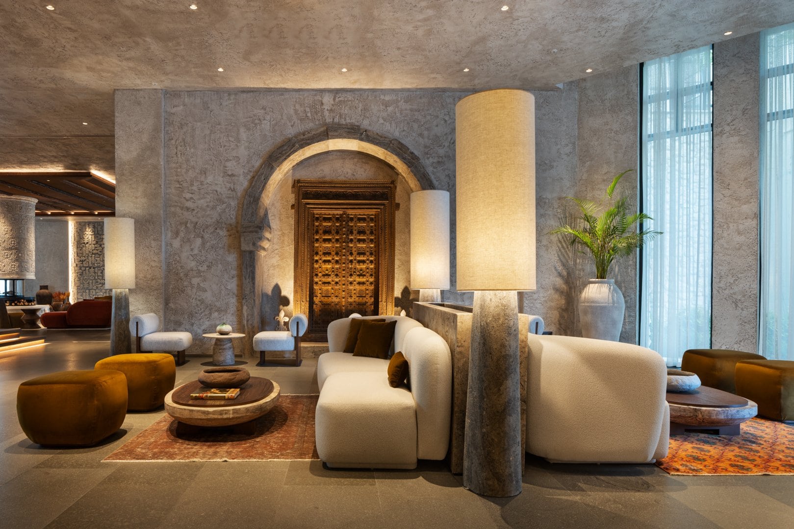 Lobby-Lounge des Hotels Fortuna of Cappadocia mit hellen gepolsterten Sofas und hohen zylindrischen Stehleuchten. Den Blickpunkt bildet eine geschnitzte Holztür in einem steinernen Rundbogen.