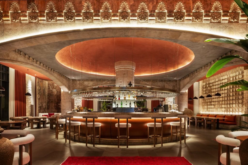 Runde Bar im Hotel Fortuna of Cappadocia mit gepolsterten Barhockern und über der Theke hängenden Gläsern. Über dem Tresen leuchtet ein kreisförmiges Deckenelement, oben verläuft ein steinernes Reliefband.