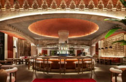 Runde Bar im Hotel Fortuna of Cappadocia mit gepolsterten Barhockern und über der Theke hängenden Gläsern. Über dem Tresen leuchtet ein kreisförmiges Deckenelement, oben verläuft ein steinernes Reliefband.