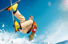 Mensch springt mit bunter Skikleidung vor blauem Himmel