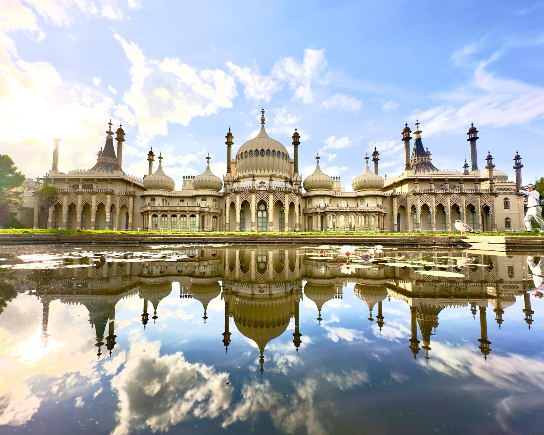 Der Royal Pavilion in Brighton, ein helles, großes Gebäude mit indisch anmutenden Kuppeln und einem großen Teich davor.