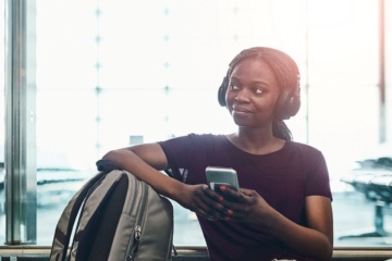 Junge Frau sitzt auf Boden im Flughafen mit Handy in der Hand