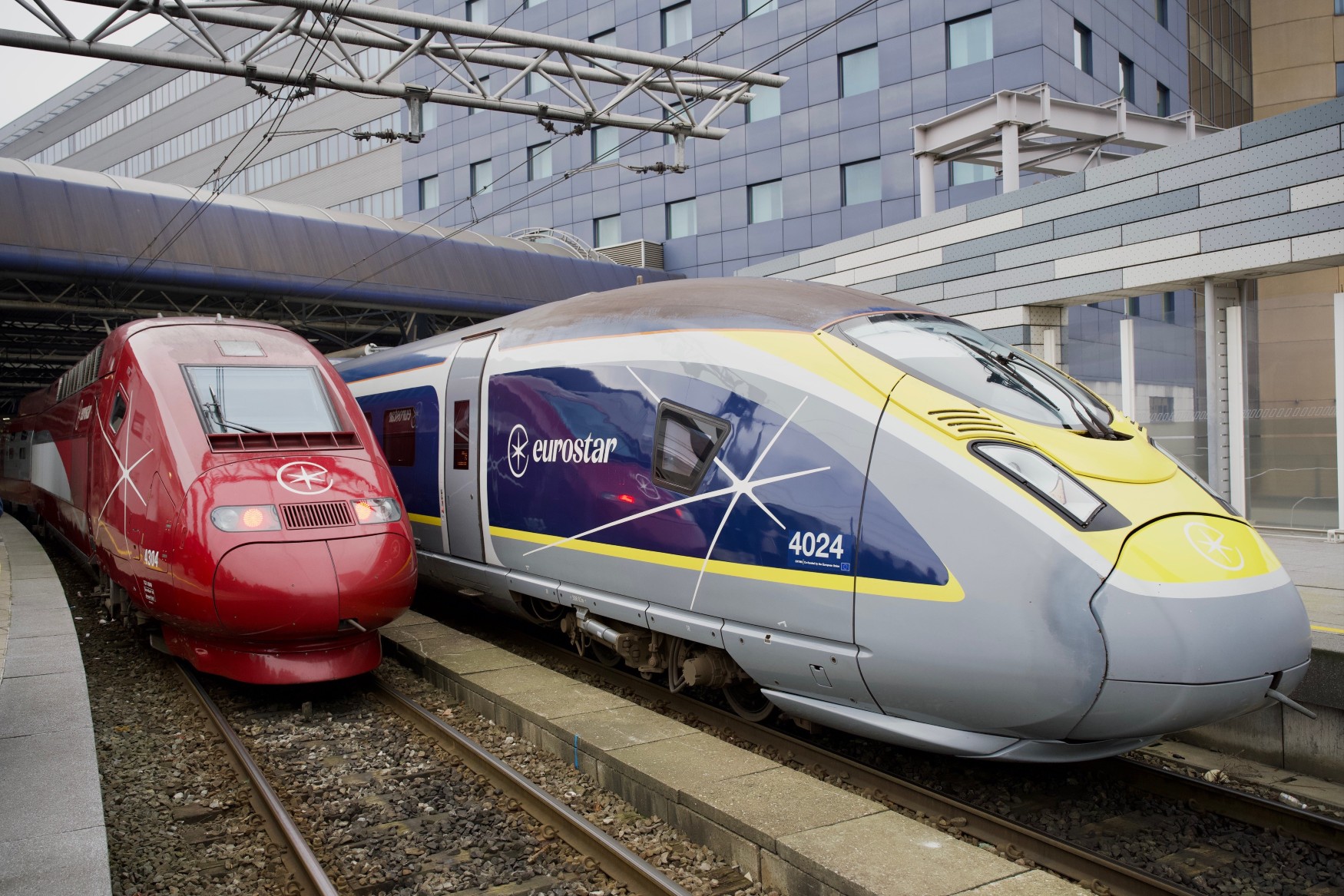 Ein roter und ein grau-blau-gelber Schnellzug, jeweils mit Eurostar-Aufdruck, stehen nebeneinander am Gleis eines Bahnhofs.