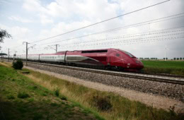 Ein roter Schnellzug mit der Aufschrift "Eurostar" fährt mit hoher Geschwindigkeit über ein Feld.