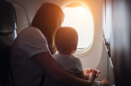 Mutter mit Kleinkind im Flugzeug im Abendlicht: Fliegen mit Baby und Kleinkind Tipps