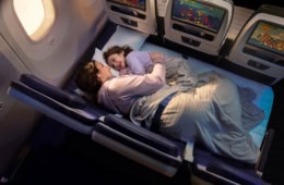 Eine Mutter und ein Kind liegen in einem Flugzeug auf einer zu einer Liegefläche umfunktionierten Dreiersitzreihe.