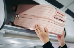 Eine Frau hebt einen Koffer in die Ablage im Flugzeug.
