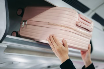 Eine Frau hebt einen Koffer in die Ablage im Flugzeug.