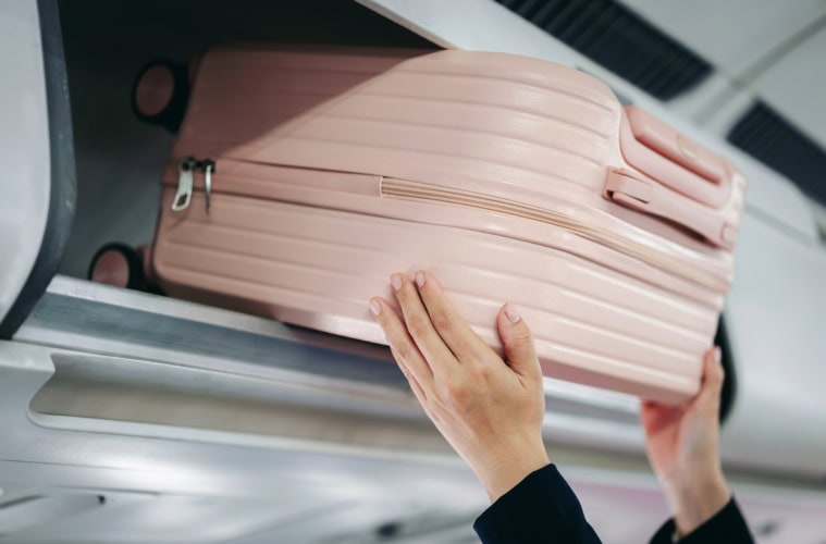Eine Frau hebt einen Koffer in die Ablage im Flugzeug.