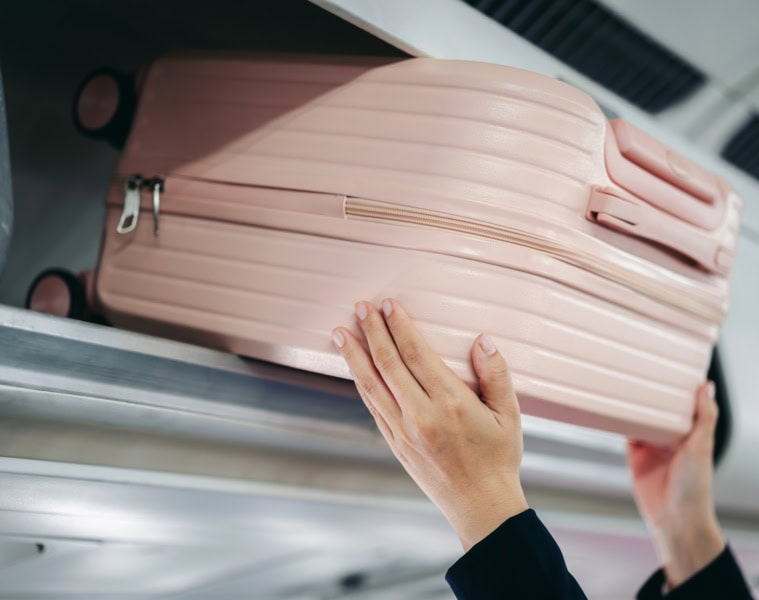 Eine Frau hebt einen Koffer in die Ablage im Flugzeug.