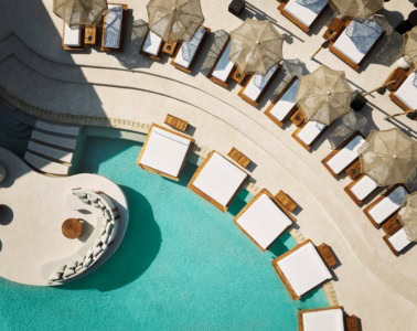 Luftaufnahme eines geschwungenen Pools in einem Resort auf Zypern. Am Rand ragen einige breite Liegen über die Wasseroberfläche.