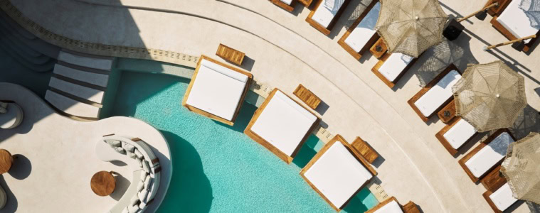 Luftaufnahme eines geschwungenen Pools in einem Resort auf Zypern. Am Rand ragen einige breite Liegen über die Wasseroberfläche.