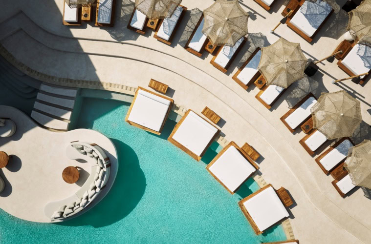 Luftaufnahme eines geschwungenen Pools in einem Resort auf Zypern. Am Rand ragen einige breite Liegen über die Wasseroberfläche.