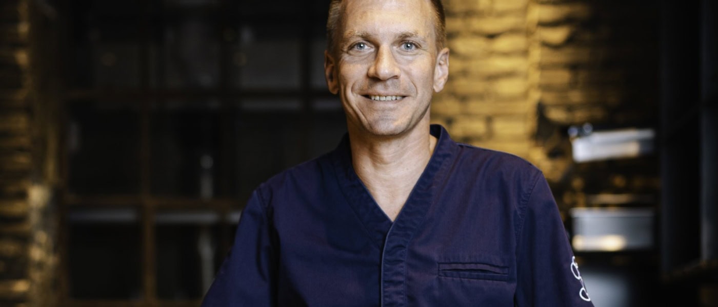 Spitzenkoch Andreas Senn in dunkelblauer Kochjacke, Porträtaufnahme vor dem Interieur des Senns Restaurant