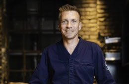 Spitzenkoch Andreas Senn in dunkelblauer Kochjacke, Porträtaufnahme vor dem Interieur des Senns Restaurant