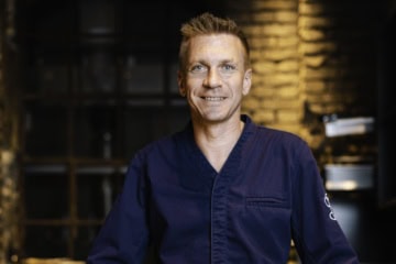 Spitzenkoch Andreas Senn in dunkelblauer Kochjacke, Porträtaufnahme vor dem Interieur des Senns Restaurant