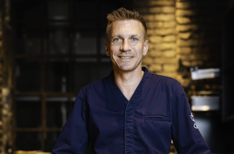 Spitzenkoch Andreas Senn in dunkelblauer Kochjacke, Porträtaufnahme vor dem Interieur des Senns Restaurant
