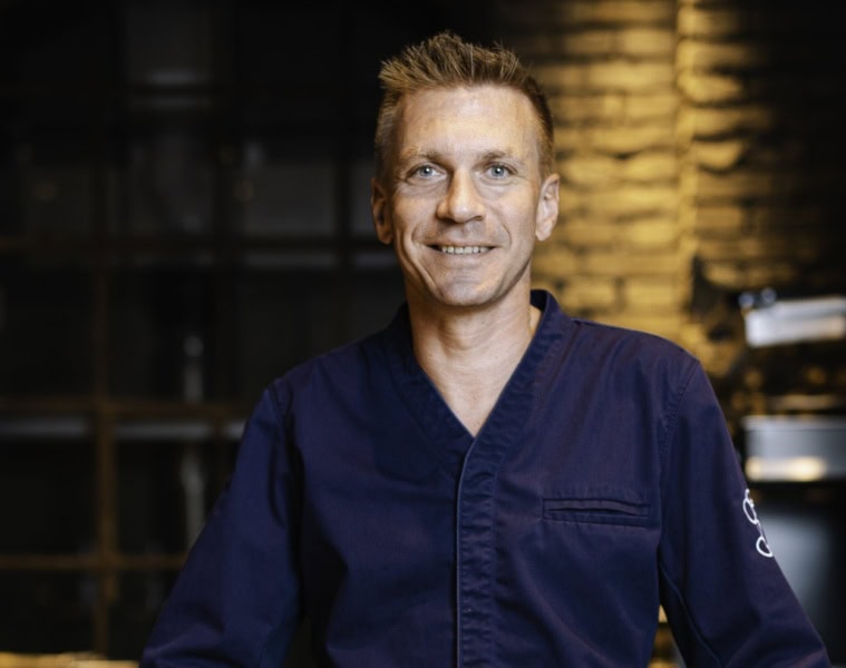 Spitzenkoch Andreas Senn in dunkelblauer Kochjacke, Porträtaufnahme vor dem Interieur des Senns Restaurant
