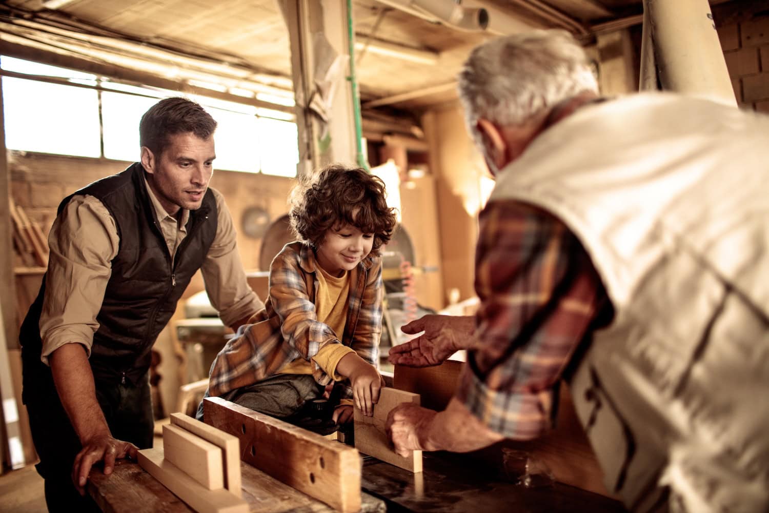 Ein älterer Mann, ein Vater und ein Kind bei einem Holzworkshop.