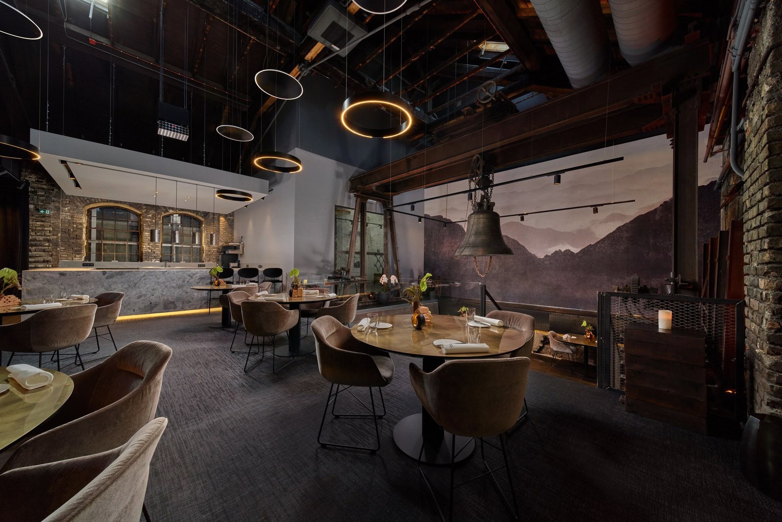 Gastraum des Senns Restaurant im Gusswerk mit runden Tischen, ringförmigen Designerleuchten und Bergpanorama-Wand