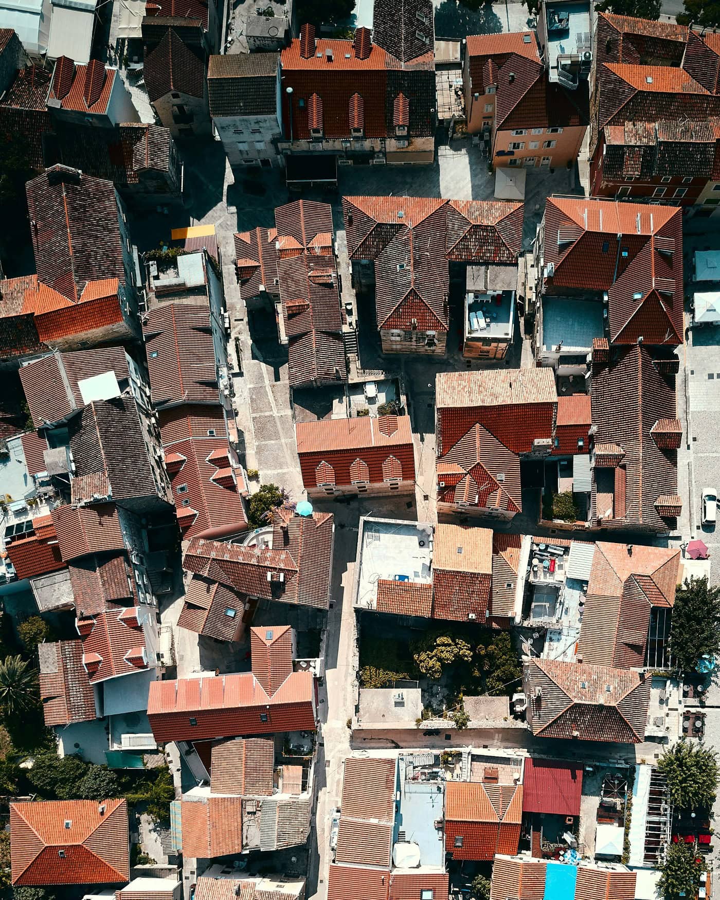 Eine mediterrane Stadt aus der Vogelperspektive; zwischen den roten Dächern der kleinen Häuschen spannt sich ein dichtes Netz aus Straßen und Gassen.