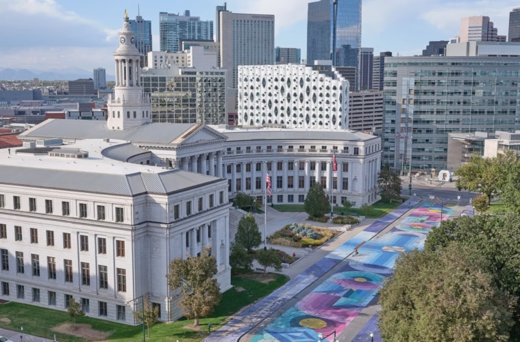 Ein halbrundes, weißes, klassizistisches Gebäude mit einem zentralen Turm: das City and County Building in Denver. Die gesamte Straße davor ist bunt bemalt.