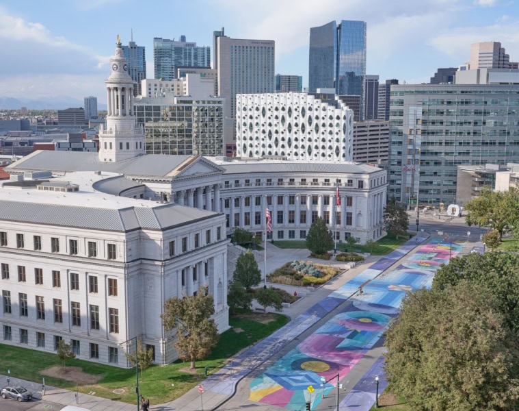 Ein halbrundes, weißes, klassizistisches Gebäude mit einem zentralen Turm: das City and County Building in Denver. Die gesamte Straße davor ist bunt bemalt.