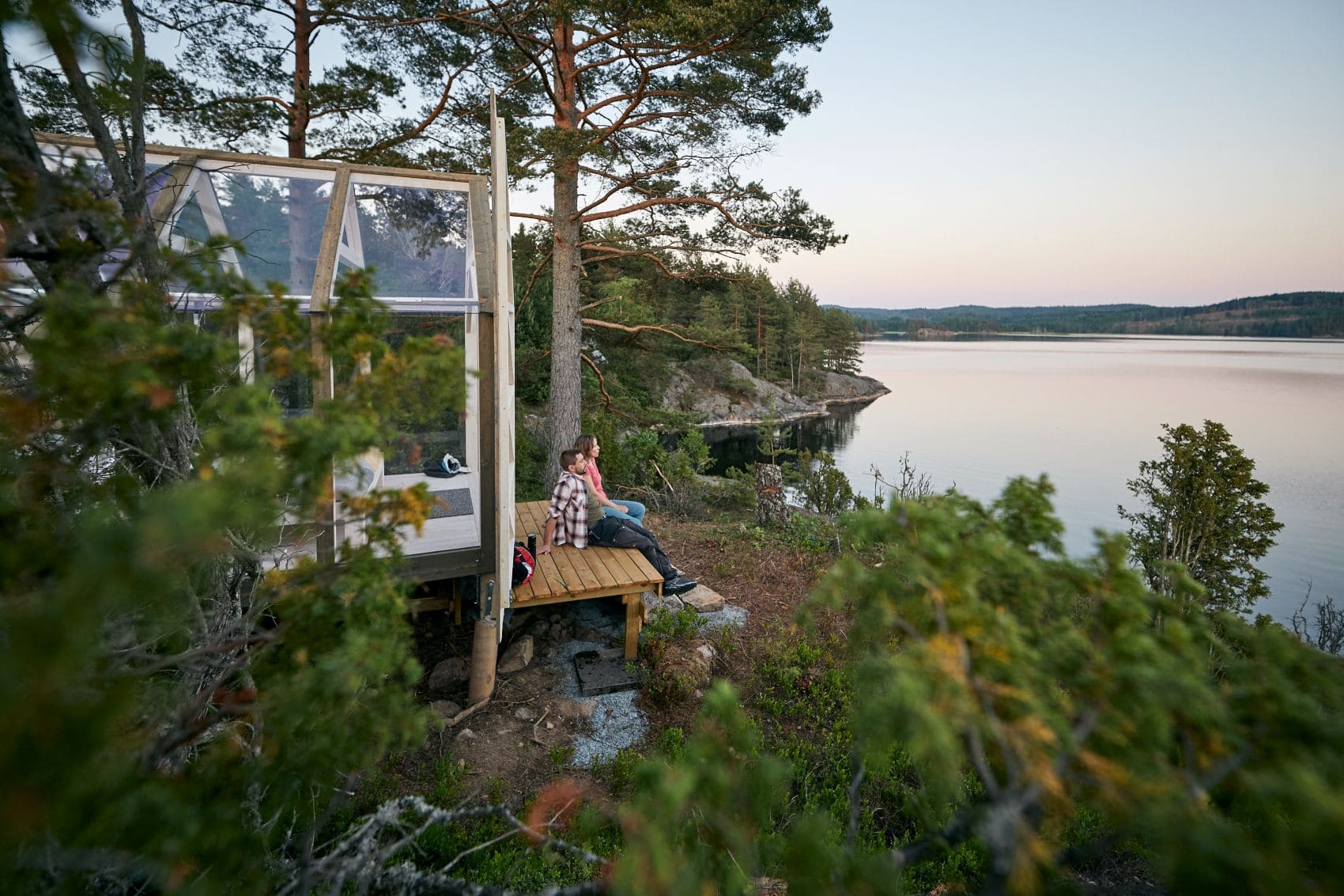 Mann und Frau sitzen vor Glashaus Steneby in Westschweden und genießen Naturausblick
