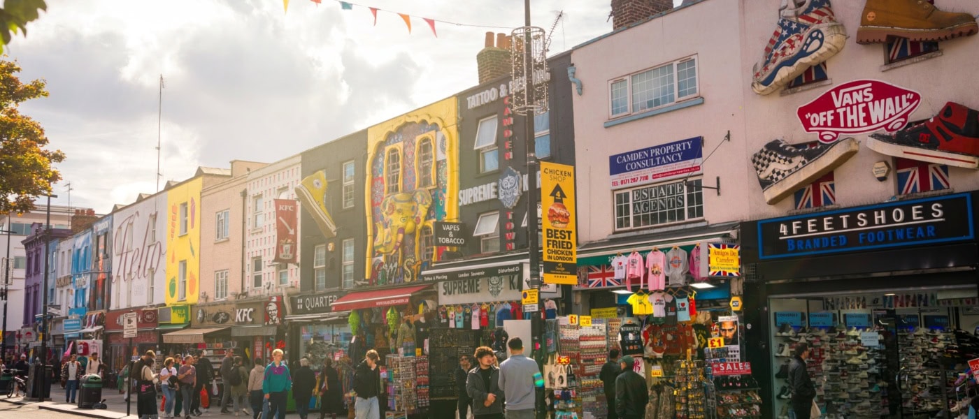 Mehrere Flachdachhäuser, jedes mit bunten, kunstvollen Murals bemalt, stehen dicht an dicht im Sommerlicht in Camden in London.