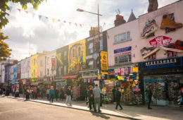 Mehrere Flachdachhäuser, jedes mit bunten, kunstvollen Murals bemalt, stehen dicht an dicht im Sommerlicht in Camden in London.