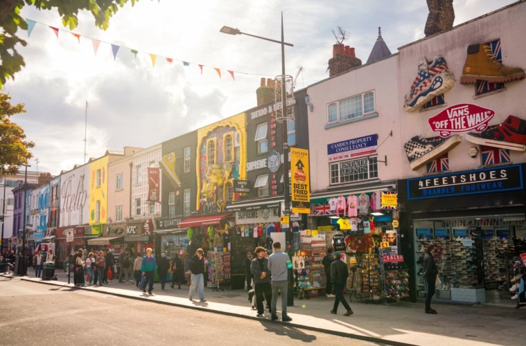 Mehrere Flachdachhäuser, jedes mit bunten, kunstvollen Murals bemalt, stehen dicht an dicht im Sommerlicht in Camden in London.