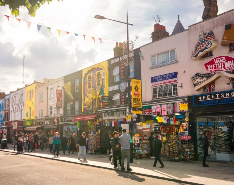 Mehrere Flachdachhäuser, jedes mit bunten, kunstvollen Murals bemalt, stehen dicht an dicht im Sommerlicht in Camden in London.