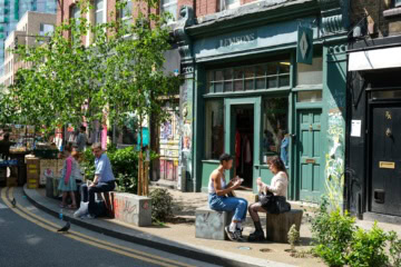 Vor einem grün angestreichenen Café in Shoreditch in London sitzen zwei junge Frauen in der Sonne und essen ein Sandwich.