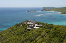 Luftaufnahme der Küste von Mustique mit Villen, dichter Vegetation und vorgelagertem Korallenriff.