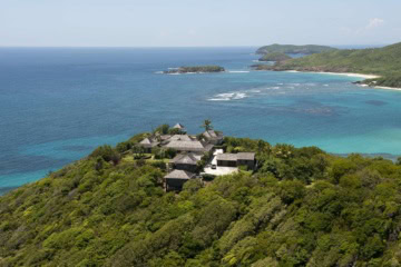 Luftaufnahme der Küste von Mustique mit Villen, dichter Vegetation und vorgelagertem Korallenriff.