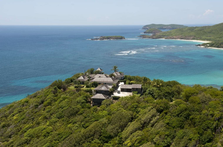 Luftaufnahme der Küste von Mustique mit Villen, dichter Vegetation und vorgelagertem Korallenriff.