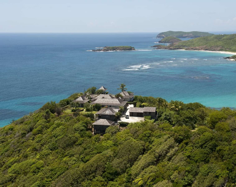 Luftaufnahme der Küste von Mustique mit Villen, dichter Vegetation und vorgelagertem Korallenriff.